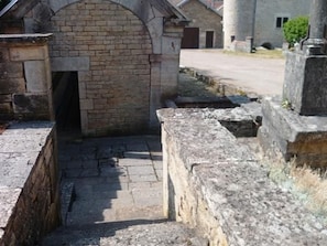 A stone pathway leading to a brick archway, with a stone wall and a cylindrical structure in the background.