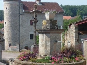 Un bâtiment en pierre doté d’une tour, d’une fontaine et d’un parterre de fleurs.