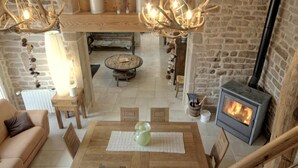 A rustic interior with a stone wall, a wooden table with chairs, a sofa, a fireplace, and a hanging light fixture. - Woodland Cottage: Comfort in Nature, near the Thousand Lakes Plateau (La Lanterne-et-les-Armonts)