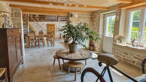 A rustic interior with a stone wall, wooden staircase, and a round wooden table with chairs. - Woodland Cottage: Comfort in Nature, near the Thousand Lakes Plateau (La Lanterne-et-les-Armonts)