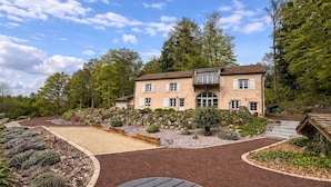 A two-story house with a stone facade, a balcony, and a landscaped garden with a gravel path and wooden furniture. - Woodland Cottage: Comfort in Nature, near the Thousand Lakes Plateau (La Lanterne-et-les-Armonts)