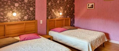 A room with two single beds, wooden headboards, floral wallpaper, pink walls, and a ceiling light fixture.