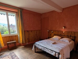 A bedroom with a wooden bed, a bench, a window with curtains, and a view of greenery outside. - Family cottage for 6 with games room and billiards (Anchenoncourt-et-Chazel)