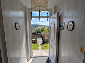 Un pasillo con una puerta que da a un jardín, un reloj en la pared y un cuadro enmarcado.