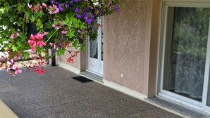 Un bâtiment avec une entrée carrelée de couleur grise, une porte blanche et une fenêtre avec un rideau.