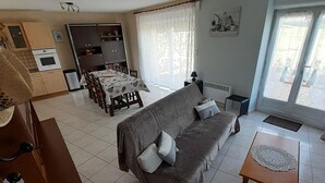 Un salon avec un canapé, une table à manger avec des chaises, un coin cuisine avec des placards et des appareils électroménagers, et une grande fenêtre avec des rideaux.