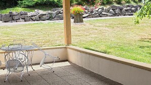 Un espace patio avec une table et des chaises, un mur en pierre et un jardin avec pelouse.