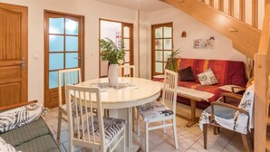 Una sala de estar acogedora con una mesa redonda de comedor, sillas blancas, un sofá rojo y una escalera.