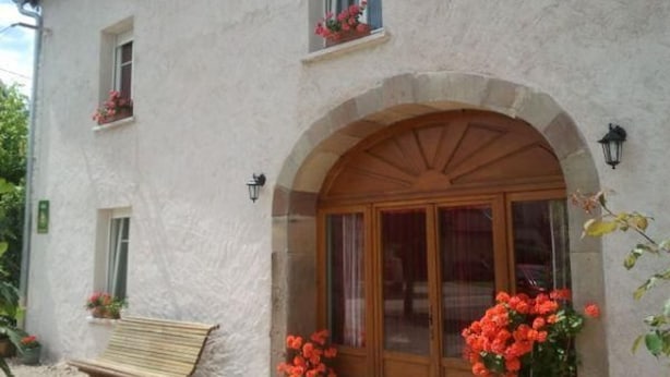 Un edificio de dos pisos con fachada blanca, una puerta de madera con paneles de vidrio y una banca en el exterior.