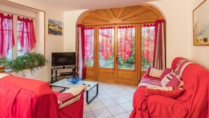 Una sala de estar con televisor, sofás rojos, una mesa de centro y un gran ventanal con cortinas.