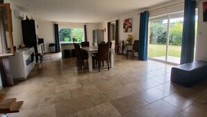 A spacious living area with a dining table and chairs, a kitchen area with a sink and cabinets, and large windows offering a view of the outdoors.