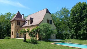 A two-story house with a swimming pool, surrounded by a well-maintained lawn and trees.