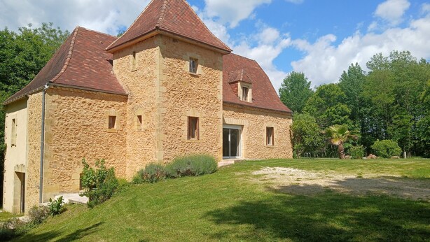 A stone building with a red-tiled roof, a large window, and a grassy lawn.