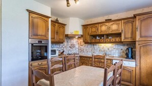 A kitchen with wooden cabinets, a dining table with chairs, a stove, an oven, and a microwave. - Charming quiet pavilion, ideal for families or friends near the Vosges (Champagney)
