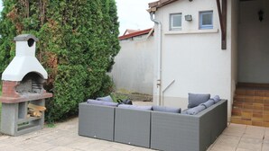 Een terras met een ingebouwde barbecue en een grijze zithoek met kussens.