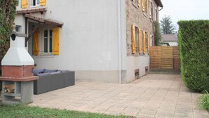 Een tweelaags huis met een geplaveid terras, een bakstenen schoorsteen en een houten omheining.