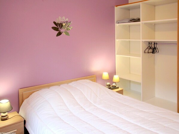 Un dormitorio con cama, lámparas de noche, una repisa en la pared y un perchero.