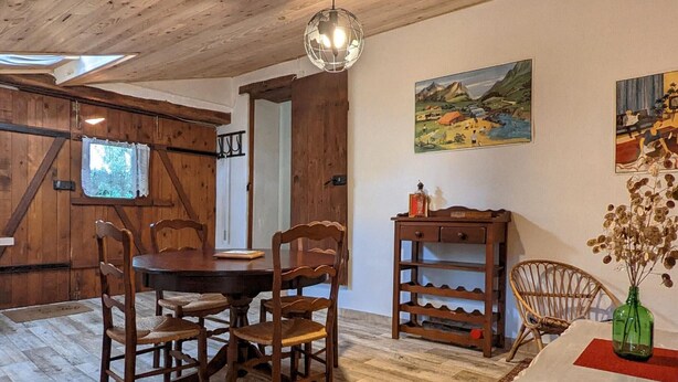 A wooden dining room with a round table and chairs, a hanging light fixture, and a painting on the wall.