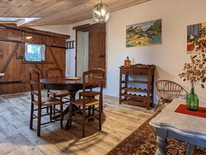 Een houten eetkamer met een ronde tafel en stoelen, een hanglamp en een schilderij aan de muur.