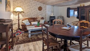 A cozy living room with a stone wall, wooden ceiling, and a round dining table surrounded by chairs.