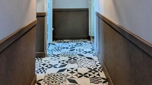 A narrow hallway with patterned black and white tiles on the floor, wooden handrails, and a door at the end.