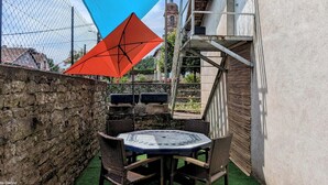 A patio area with a round table and chairs, a blue and red canopy, and a stone wall.