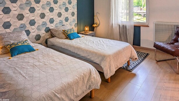 A bedroom with two beds, a nightstand, a lamp, a chair, and a window with curtains.