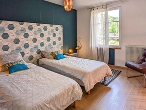 A bedroom with two beds, a nightstand, a lamp, a chair, and a window with curtains.