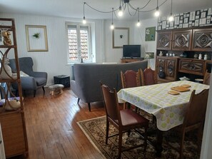 En stue med sofa, spisebord med stole, fjernsyn og et skab med pynt.