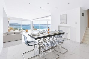 A modern kitchen with a large island, white cabinetry, and a view of the sea. - Villa Infinity (Megara)