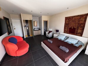 Un dormitorio moderno con una cama grande, una silla roja, un vestidor y un baño con ducha y lavamanos.