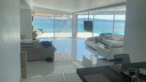Een moderne woonkamer met een grote glazen deur die leidt naar een balkon met uitzicht op een wateroppervlak.
