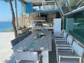 Un área de comedor al aire libre con pared de piedra, una parrilla y vistas al mar.