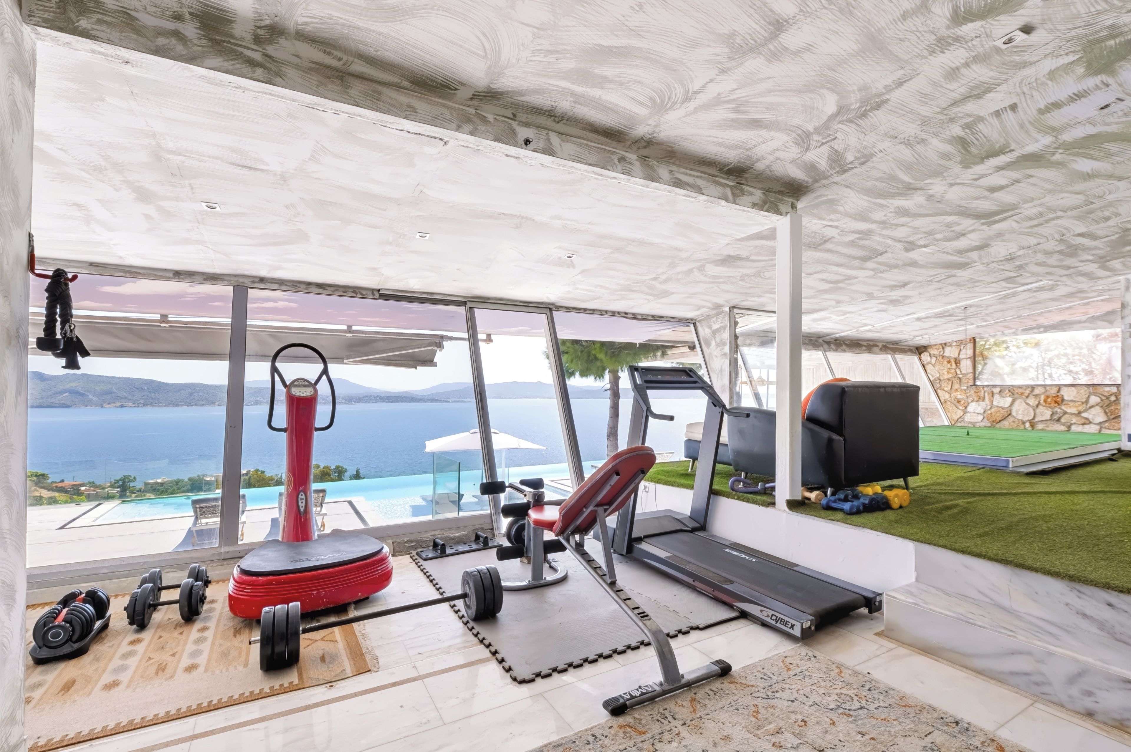 A home gym with exercise equipment, a treadmill, and a view of the sea.