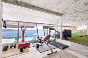 A home gym with exercise equipment, a treadmill, and a view of the sea.