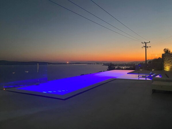 Terraza en la azotea con piscina y sillones de descanso, con vistas a un cuerpo de agua y al horizonte urbano al anochecer.