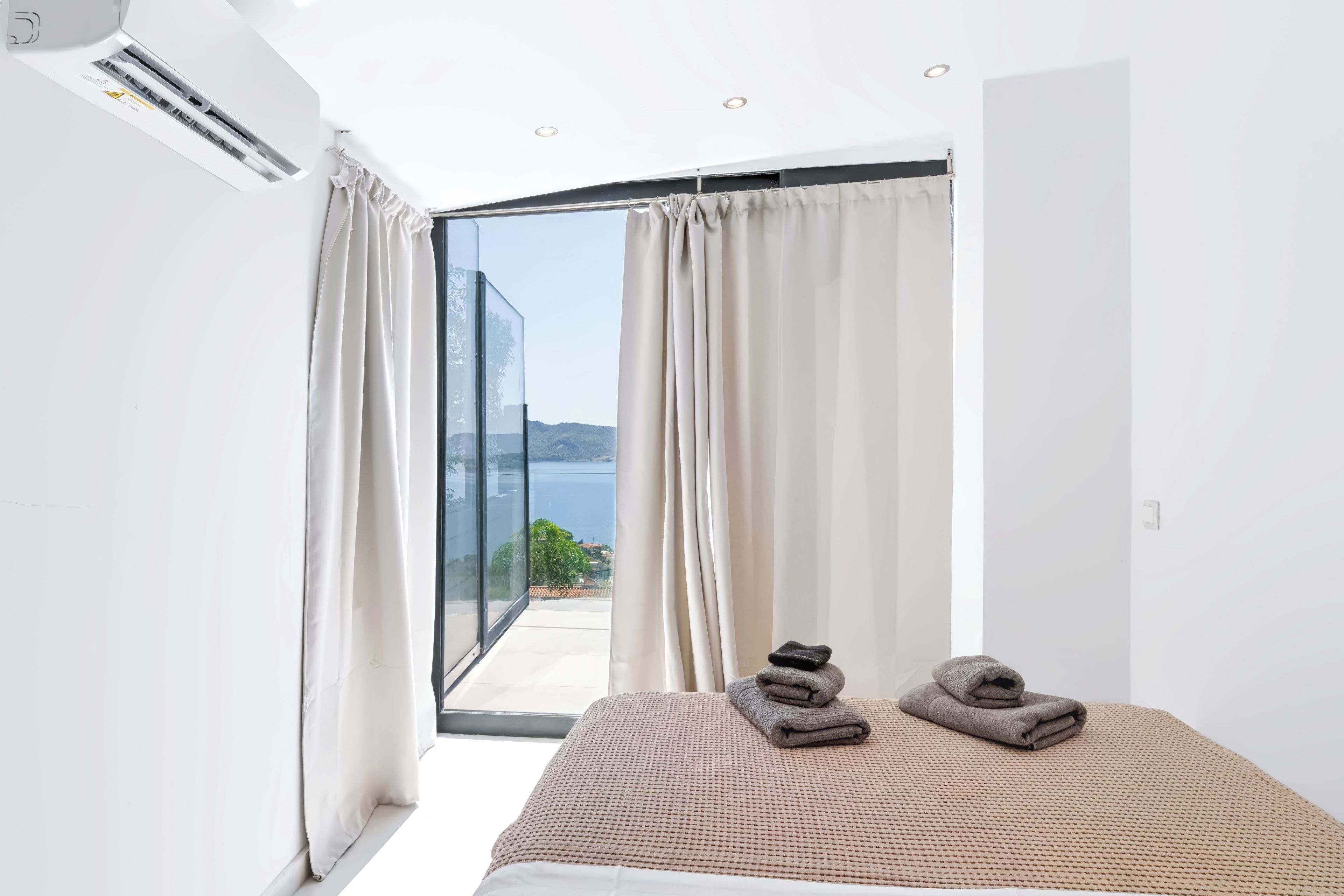 A bedroom with a bed, a view of the sea, and a balcony with curtains.