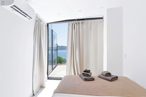 A bedroom with a bed, a view of the sea, and a balcony with curtains.