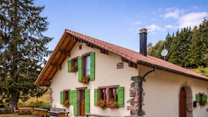 A traditional chalet with a sloped roof, stone foundation, and green shutters.
