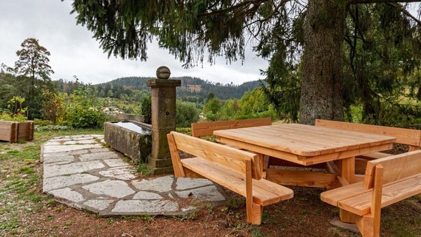 An outdoor wooden table and benches, a stone pathway, and a view of a forested landscape.