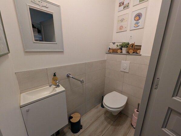 A small, modern bathroom with a sink, mirror, toilet, and a small trash bin.