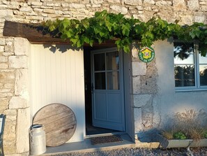 A stone building with a wooden door and a metal barrel outside.