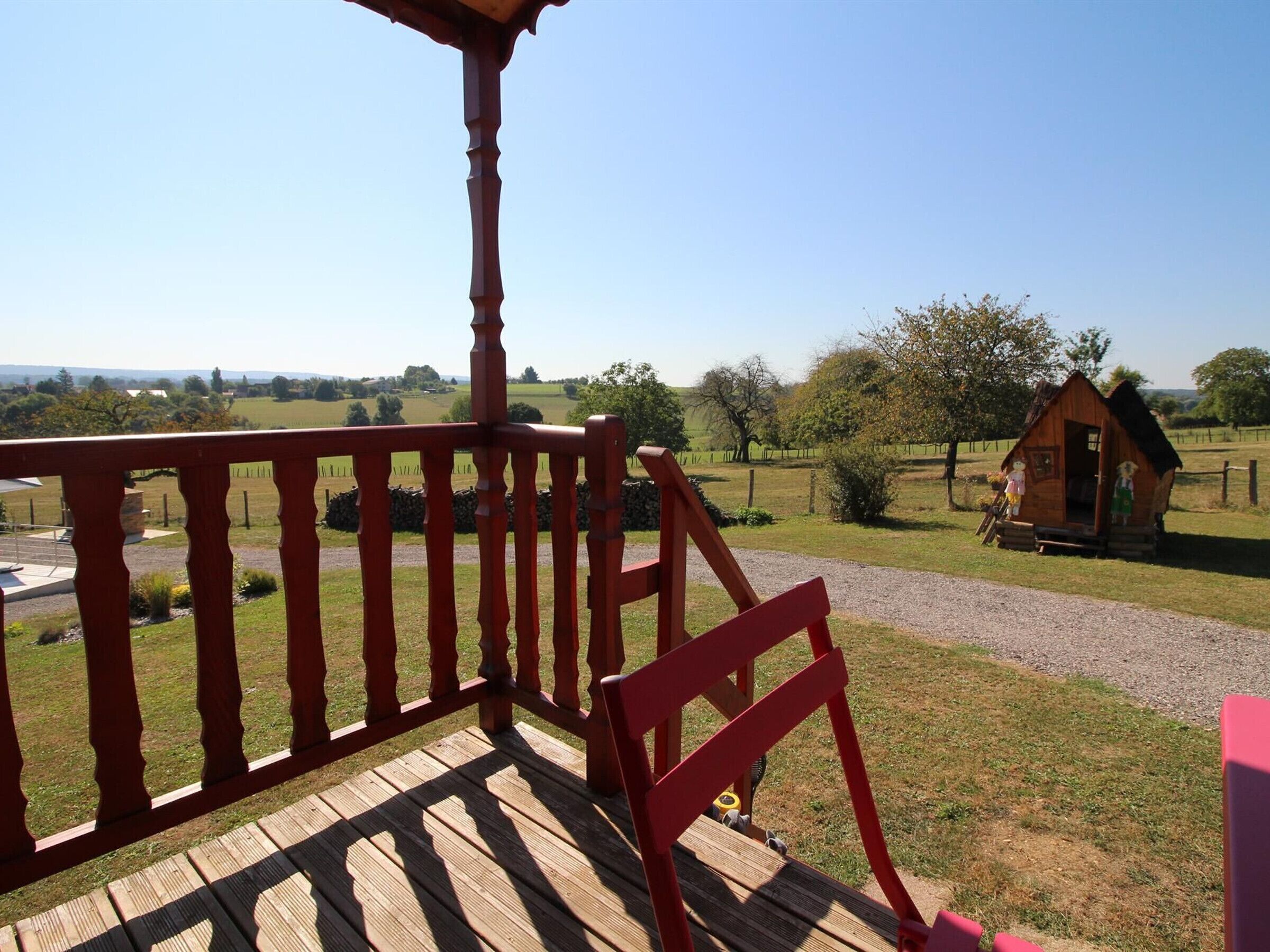 A wooden deck with a red railing overlooking a rural landscape.