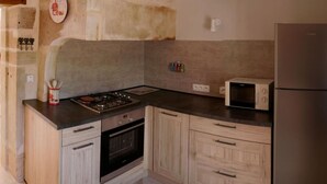Una cocina con estufa a gas, horno, microondas y refrigerador. Hay armarios de madera y un reloj en la pared.