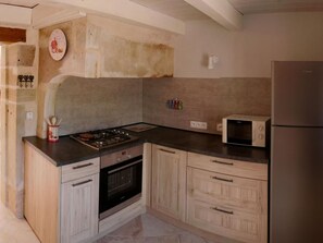 A kitchen with a gas stove, oven, microwave, and a refrigerator. There are wooden cabinets and a clock on the wall. - Secluded Cottage 6 Pers. Pets Allowed (La Rosière)
