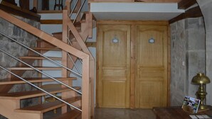 Una escalera de madera que conduce a un segundo piso, una puerta de madera con manija y una pequeña mesa con una lámpara y un folleto.