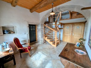 A rustic interior with a wooden staircase, a red upholstered chair, and a dining table with ceramic dishes.
