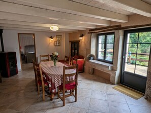 A dining area with a table set for four, wooden chairs, a vase with flowers, and a view of greenery through a window.