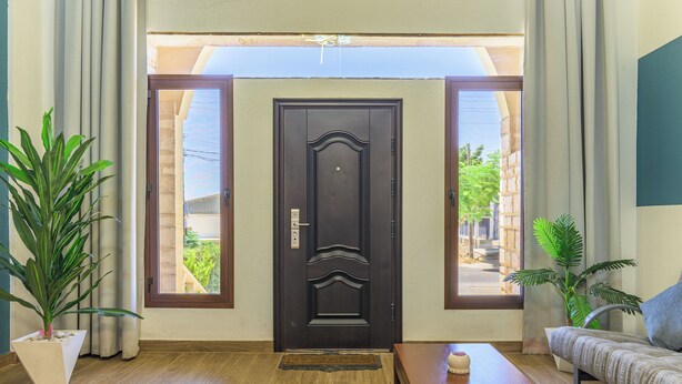A room with a dark wooden door, a wooden floor, a sofa, a coffee table, and two potted plants. - Mavi 1BR Apartment With Jacuzzi In Batroun (Batroun)
