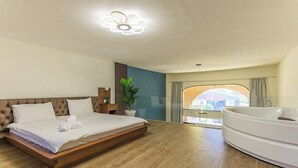 A modern hotel room with a large bed, a bathroom with a bathtub, and a view of the city through a window. - Mavi 1BR Apartment With Jacuzzi In Batroun (Batroun)